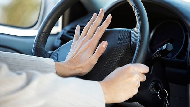 woman pressing car horn on steering wheel 